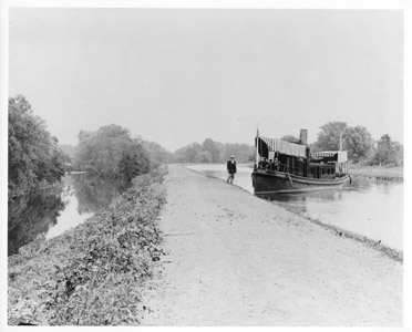 Mr. George Holcombe, Paymaster of the Delaware and Raritan Canal Company, stands next to the steam yacht Relief in this photograph taken north of the City of Lambertville in the year 1892.   Constructed in Camden and launched in 1884, the Relief was used by the Delaware and Raritan Canal Company as a pay-boat and traveled the length of the canal monthly to disburse wages to company workers.  